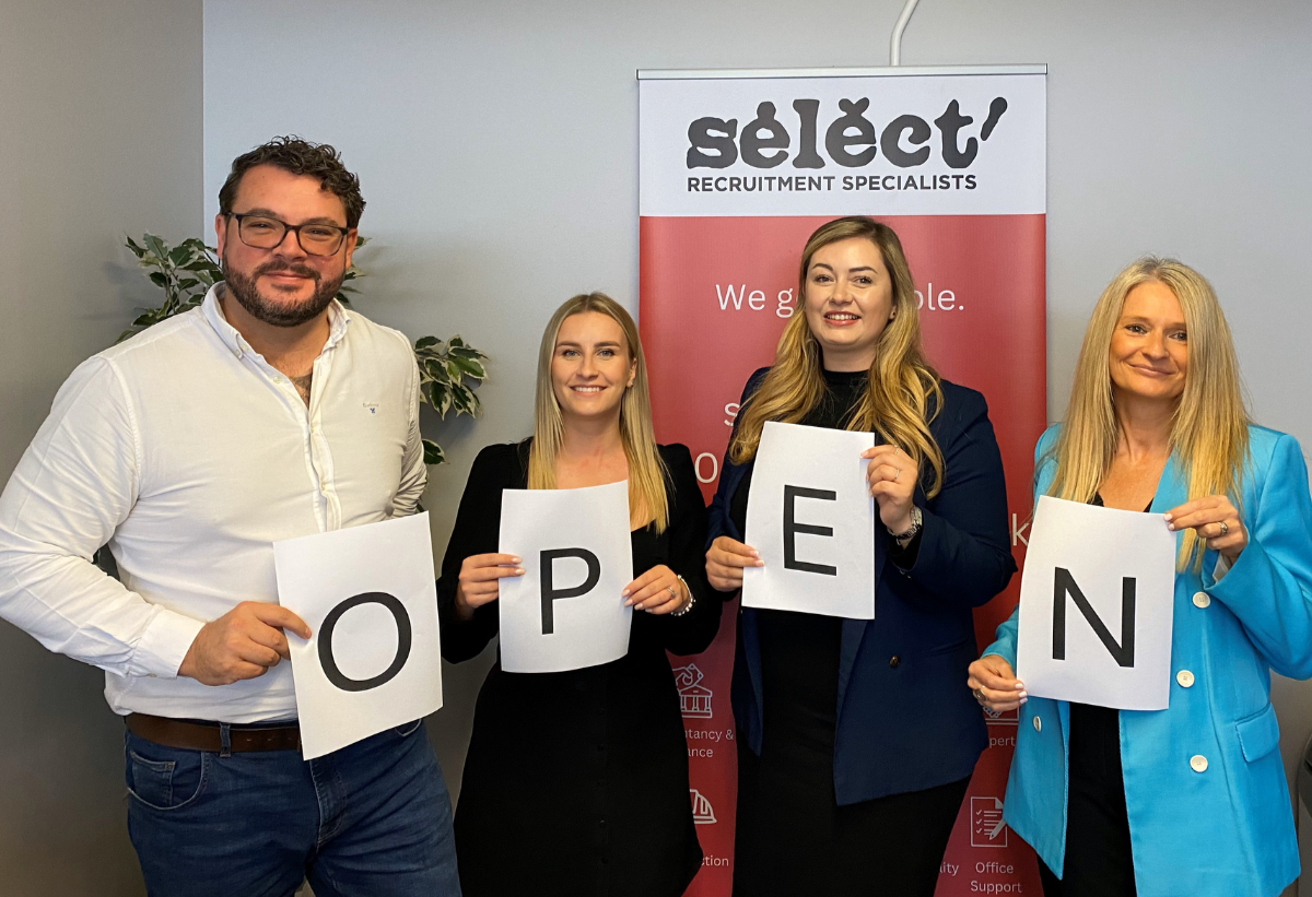 4 people holding a piece of paper each. The pieces of paper each have one letter on them, that together spell the word "Open"