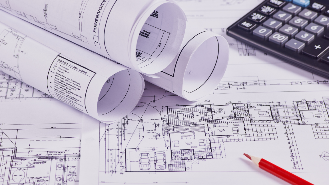 An image of construction blueprints on a table. There are several more rolled up blueprints on top.