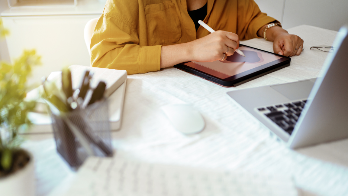 An image of a designer drawing a graphic on digital tablet, sat at a white desk.