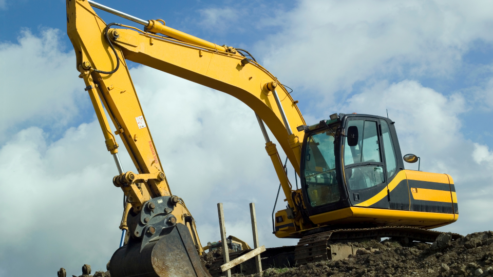 An image of a 360 excavator machine on a construction site. The machine is on top of a mound of earth, and is using the scoop to move more earth.