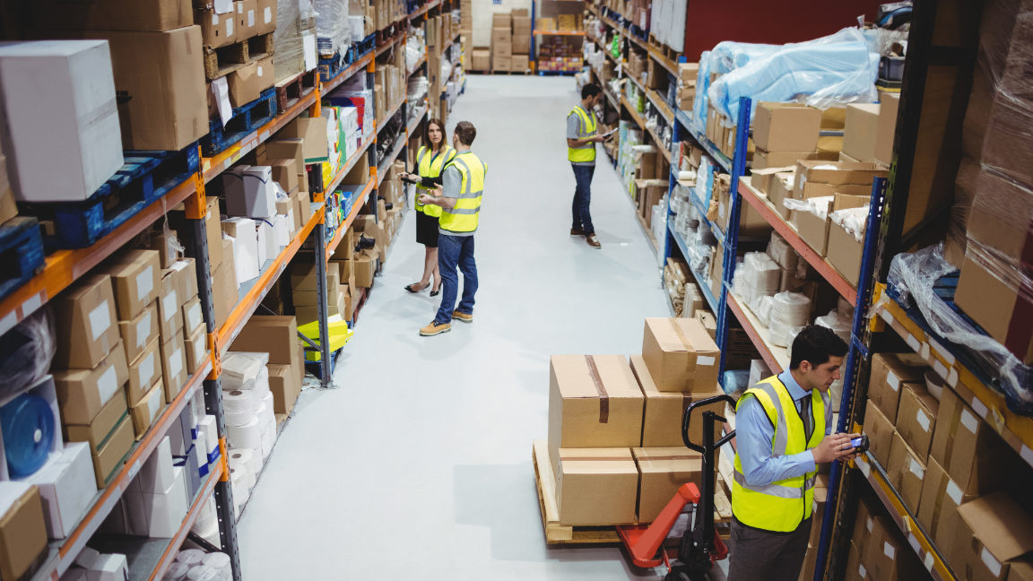 An aerial shot of workers in a warehouse looking for products on shelves. They are using PDAs to find the products.