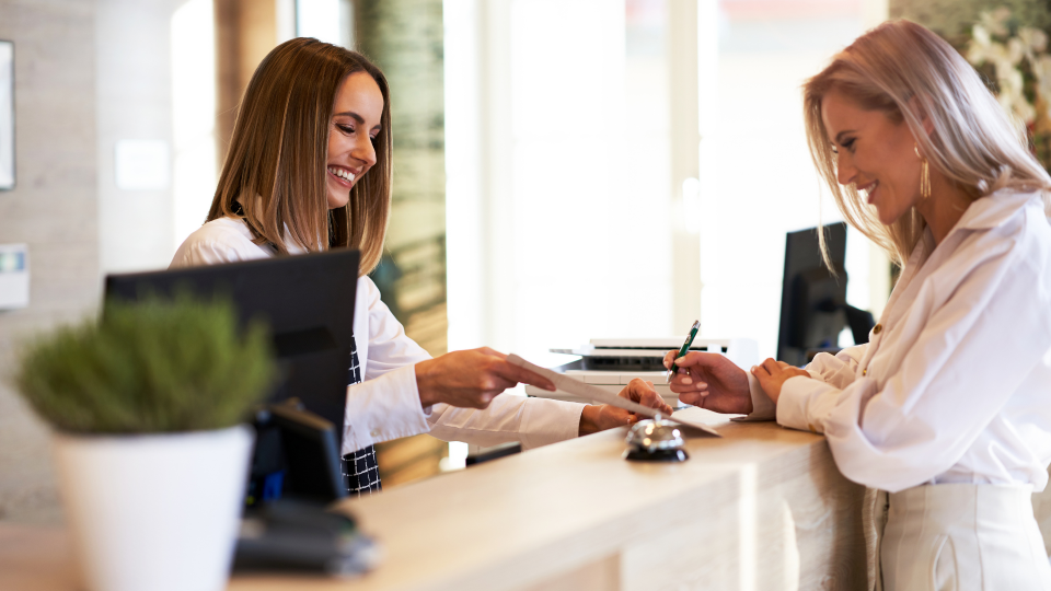 An image of a receptionist helping a customer complete some forms.