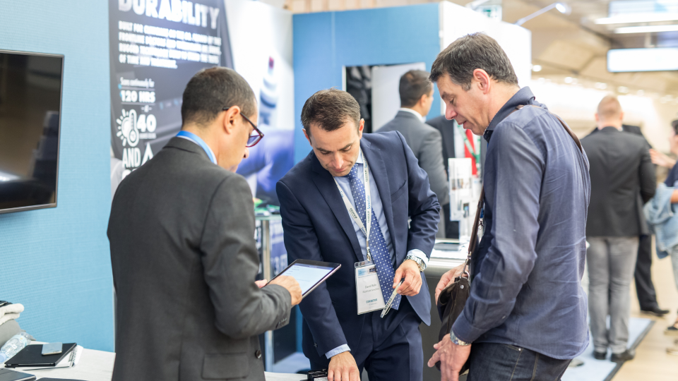 An image of three men at a product convention event. They are looking at a product in a stall