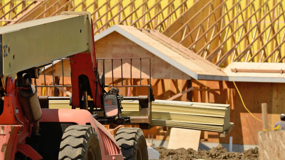 A telehandler carrying a load of construction materials towards a building under construction