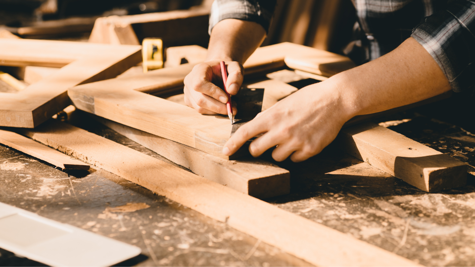 An image of a carpenter measuring and marking a piece of wood. He is using a pencil and metal ruler