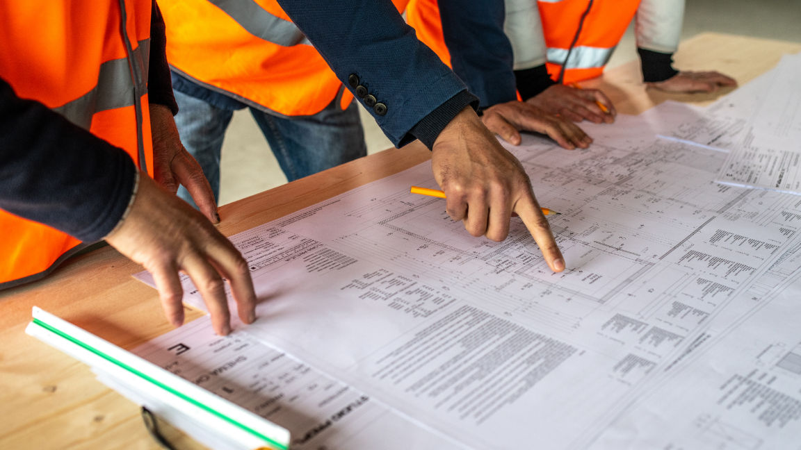 Three construction workers looking at construction plans. They are wearing high-visibility jackets