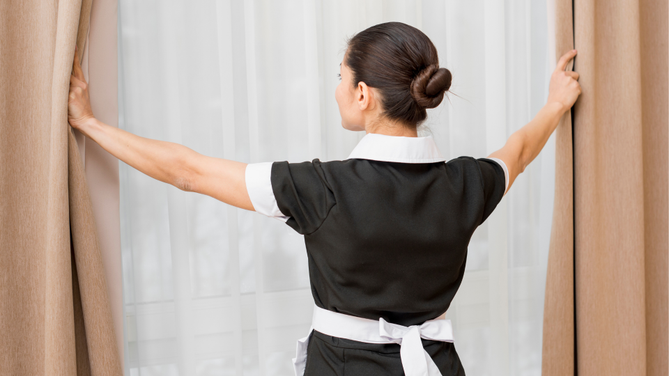 An image of a hotel housekeeper checking the curtains and windows in a hotel room