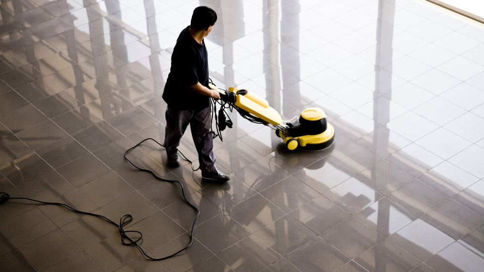 A high-angle image of a cleaner using a floor-buffer to clean and polish a tiled floor