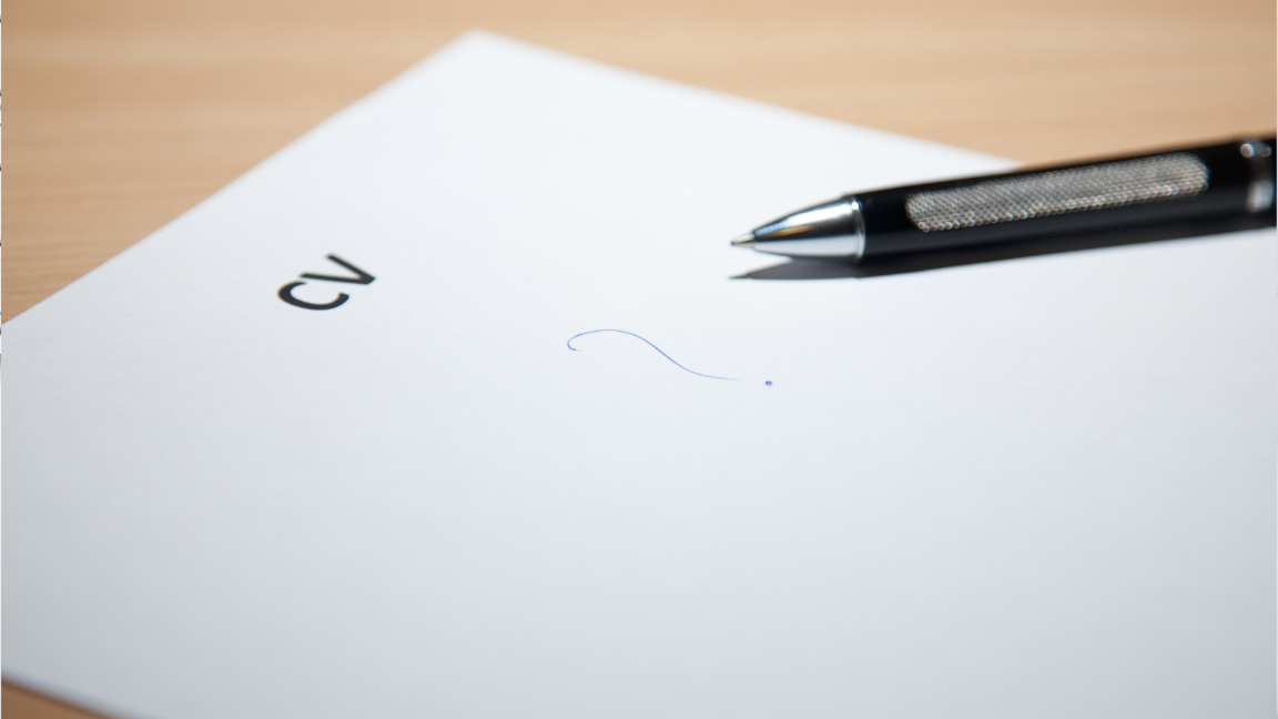 A close up image of a piece of paper on a desk. The paper has "CV" printed on the top, and a hand-drawn question mark in the middle, with a pen resting next to it.