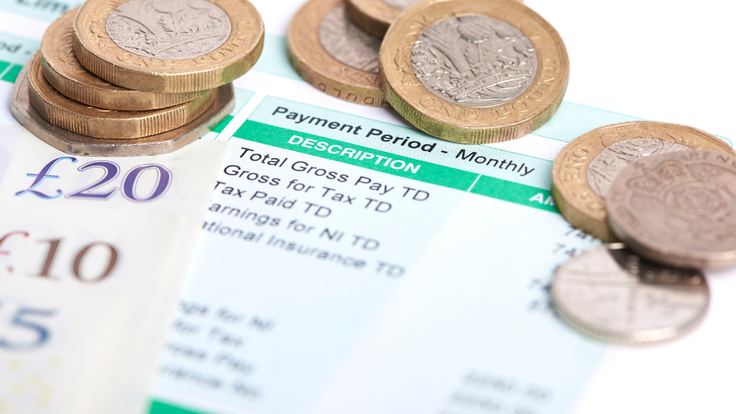 A close up image of a pay slip. There are various British coins and bank notes on top of the image