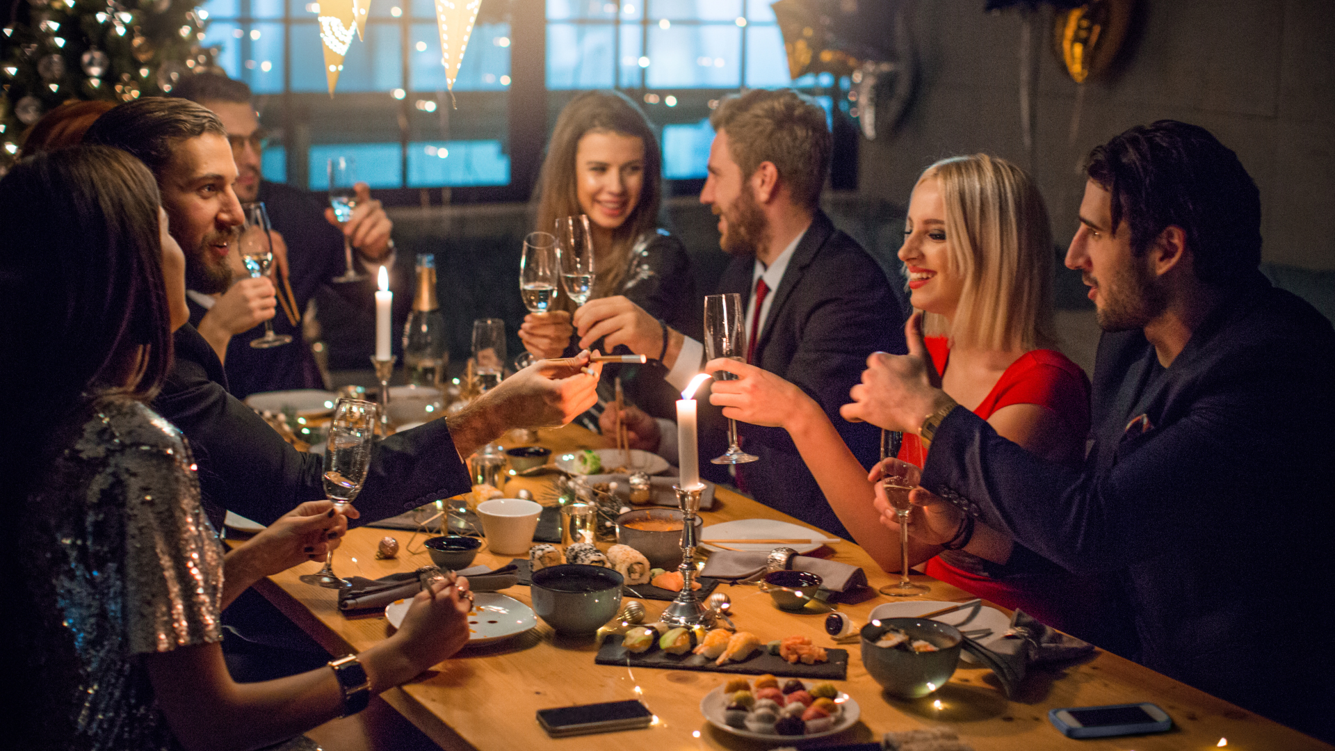 An image of people enjoying a christmas meal in a restaurant. They are wearing formal party wear, and drinking from wine glasses. There is food and plates on the table.