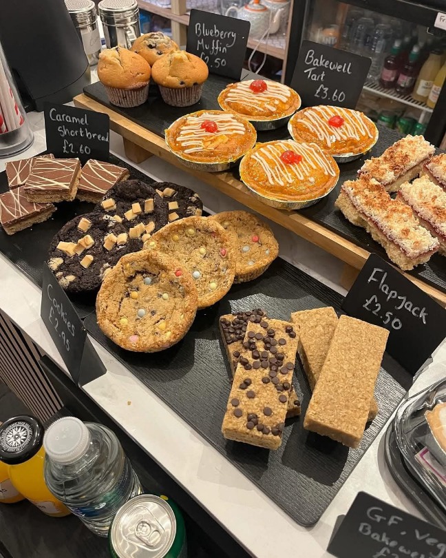 An image of the cakes and pastries available at Attic Brew, with their prices included. The offerings include flapjacks, cookies, muffins, and tarts