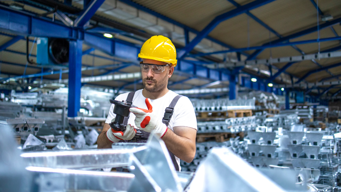 A man inspecting newly manufactured items. He is wearing a hard-hat an eye protection.