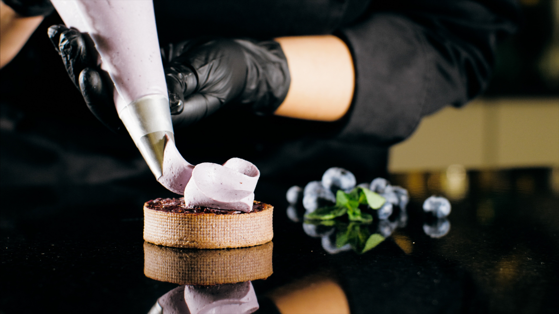 A Pastry Chef pipping a decorative layer of cream on top of a tart