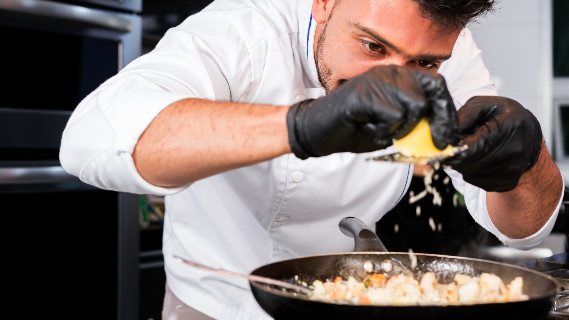 A chef grating a lemon over a frying pan. The frying pan contains prawns and other ingredients