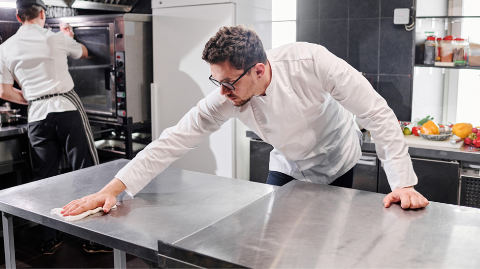 A kitchen assistant cleaning work surfaces  in a commercial kitchen