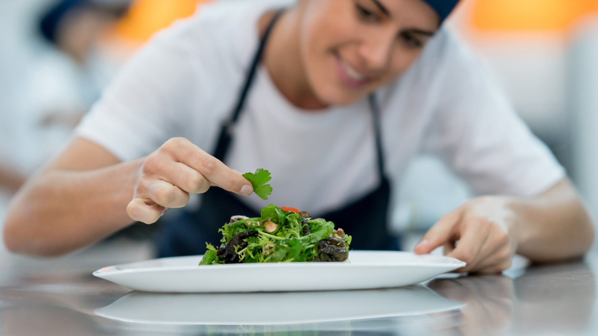 A chef adding garnished to a meat dish on a white plate.