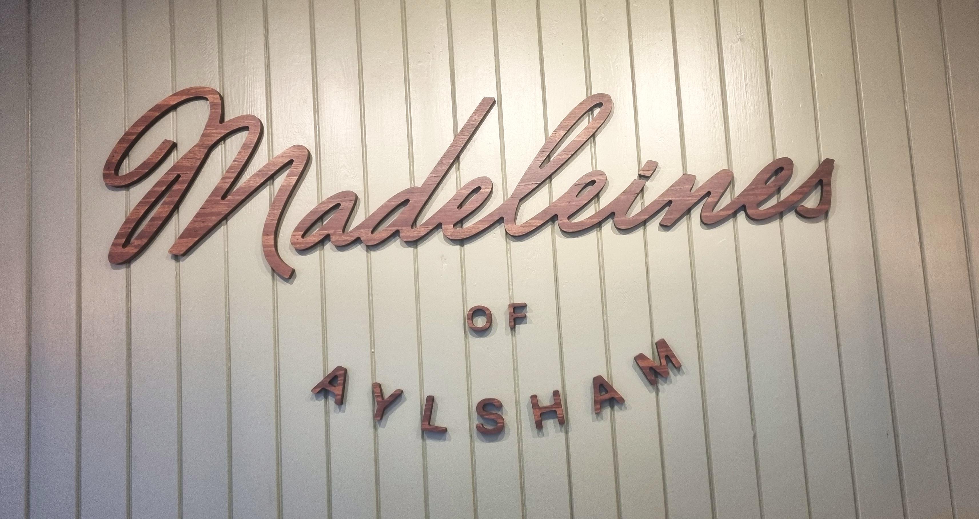 A picture of the sign for Madeleines cafe, it is composed of brown wood on a green wooden wall