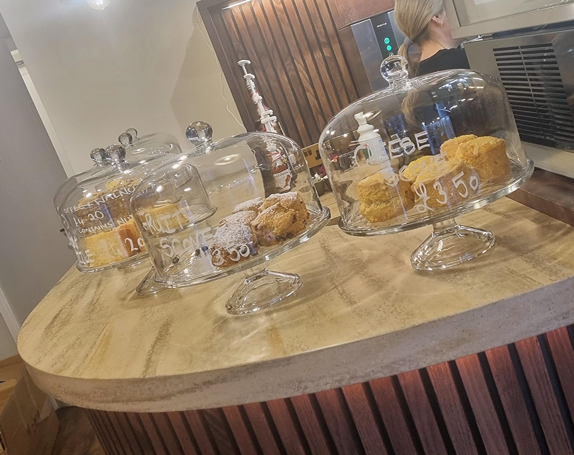 A selection of sweet treats available to purchase at Madeleines. They are on glass cake stands, under cloches with the price and name of the product written on them