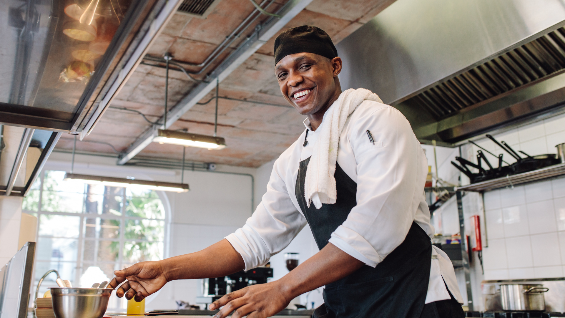 A male chef working in a restaurant kitchen. He has a towel over his shoulder and is smiling