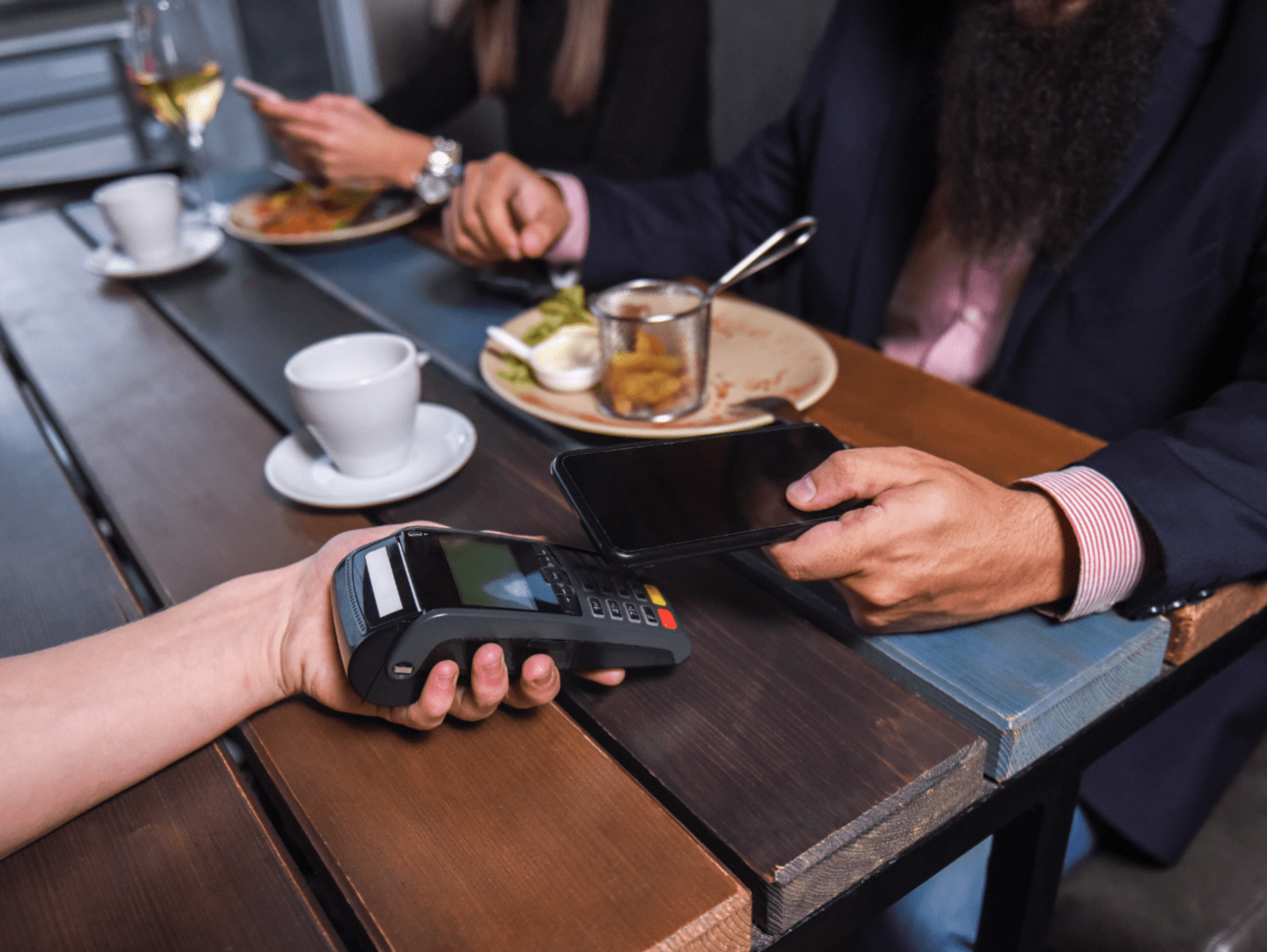 A couple paying for a meal at a restaurant. They are using a mobile phone to pay via contactless