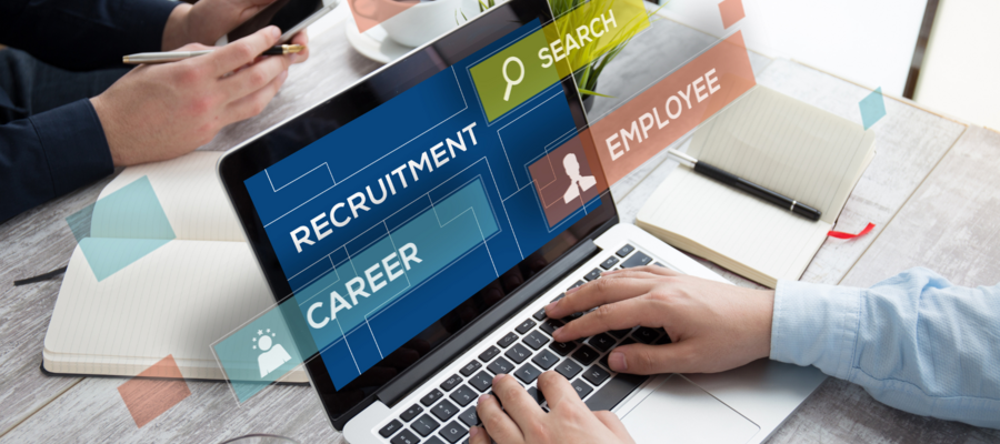 A laptop on a wooden desk, with the words "Recruitment", "Search", "Career", and "Employee" on the screen.