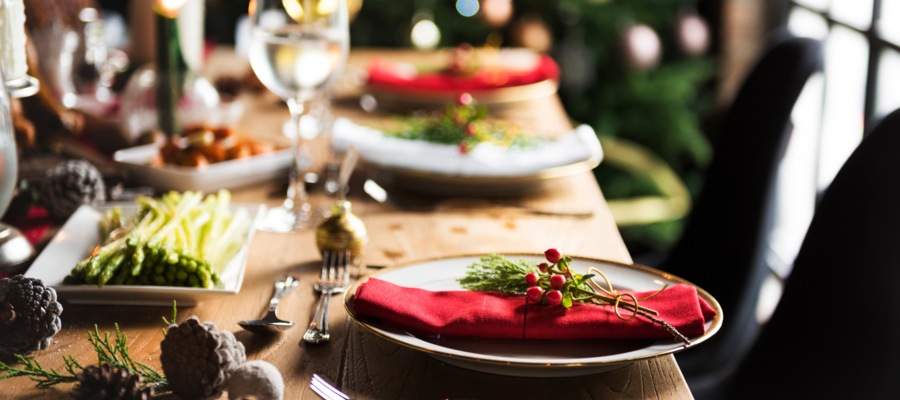 An image of a table in a restaurant that has been prepared for a christmas meal. There are christmas decorations on the table, and red napkins on the plates, with a holly decoration