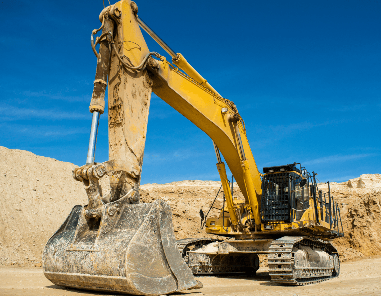 An image of a 360 excavator machine on a construction site. The machine is in a sand pit, and there is a clear blue sky in the background.