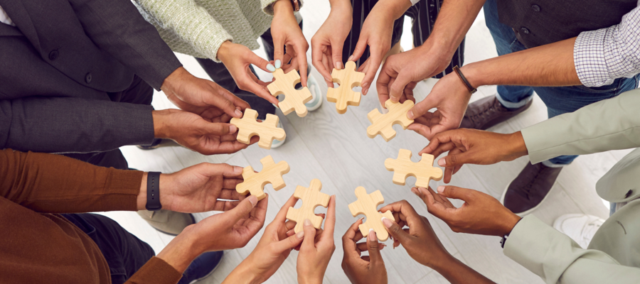 8 pairs of hands holding jigsaw pieces together in the shape of a circle