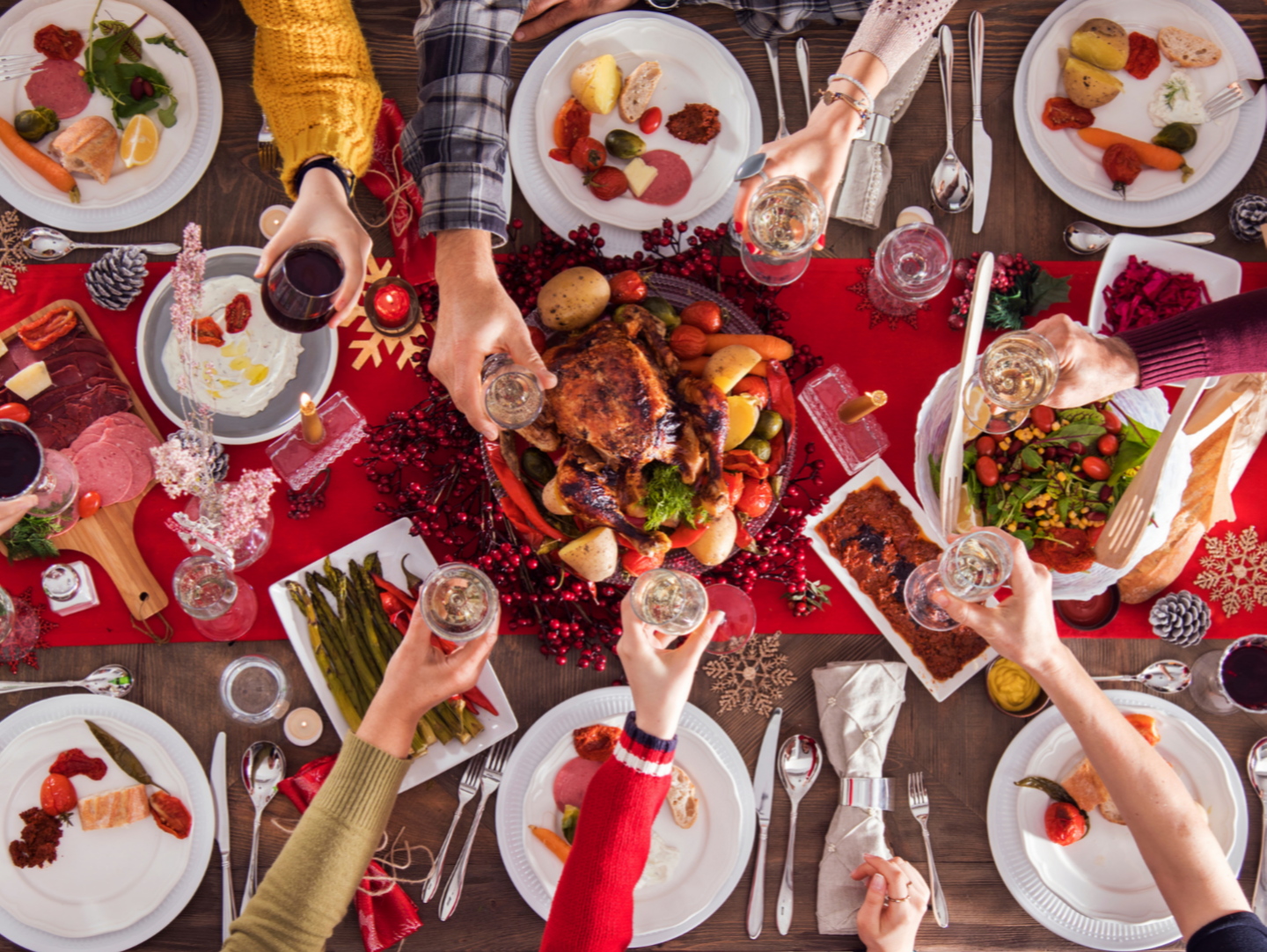 An overhead shot of people enjoying a christmas meal. There is an assortment of christmas foods on the table, and the people are raising their wine glasses in a toast