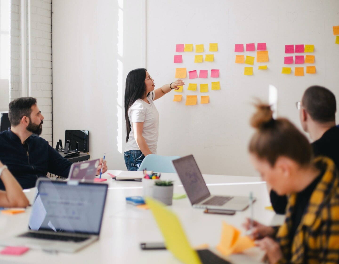 An image of workers in a marketing agency in a meeting. One person is pointing at information on the whiteboard, the others are sat around a conference table.