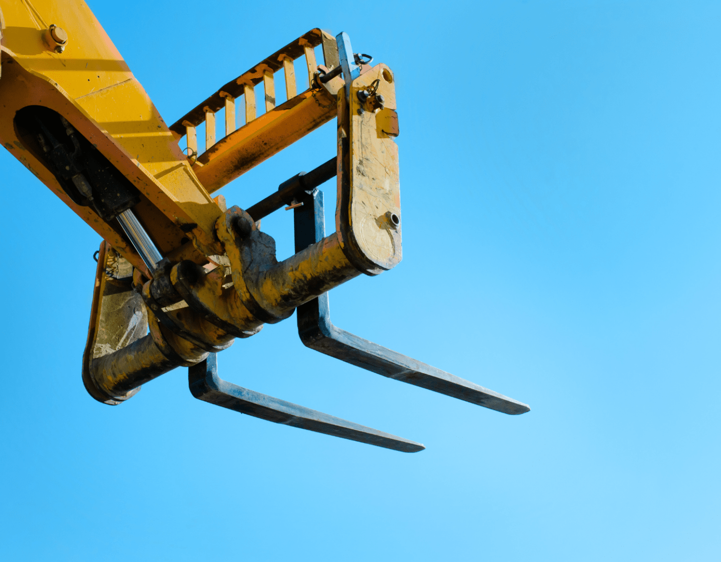 The fork end of a telehandler against a blue sky