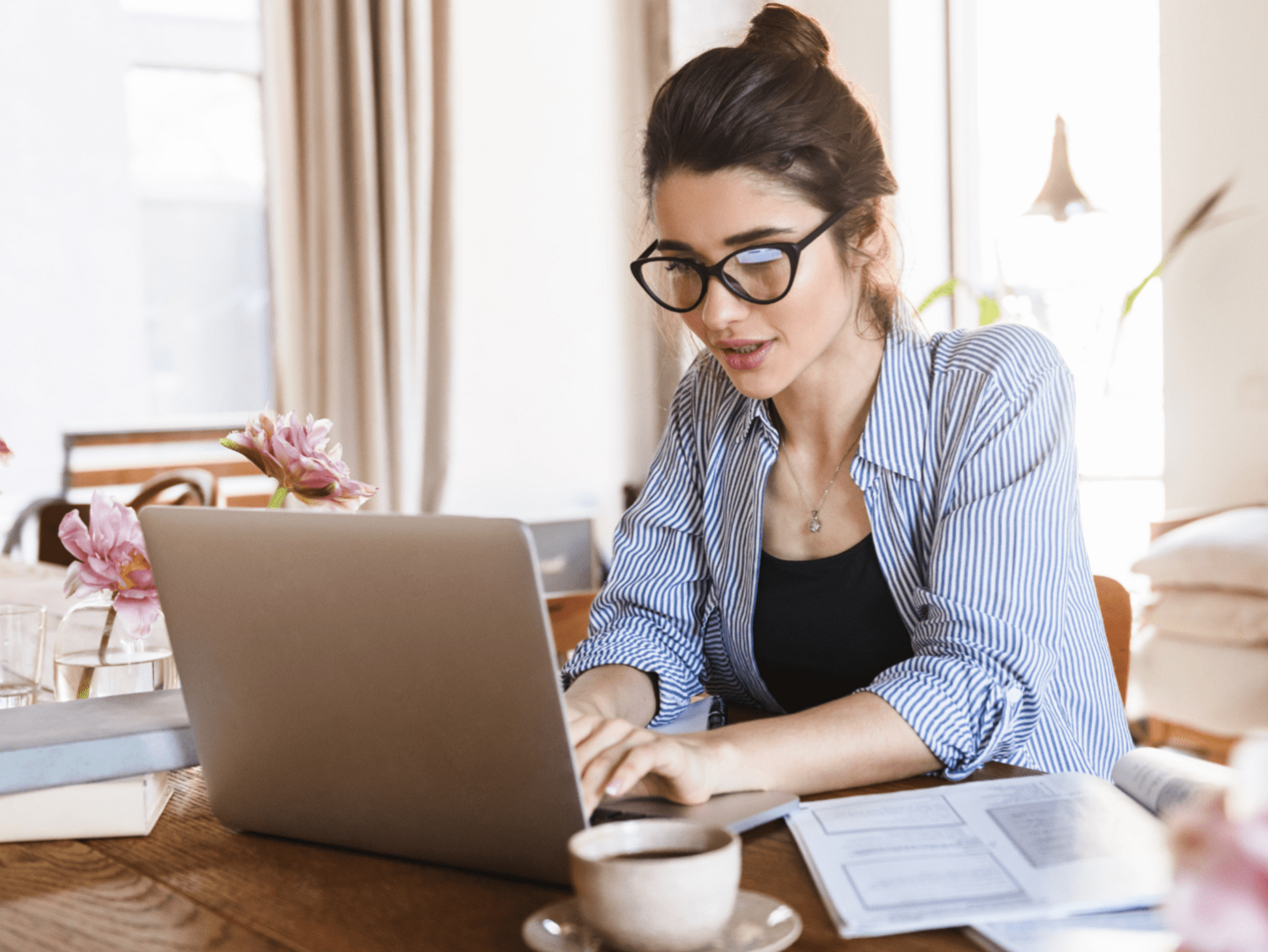 A woman working from home. She is using a grey laptop placed on a wooden desk