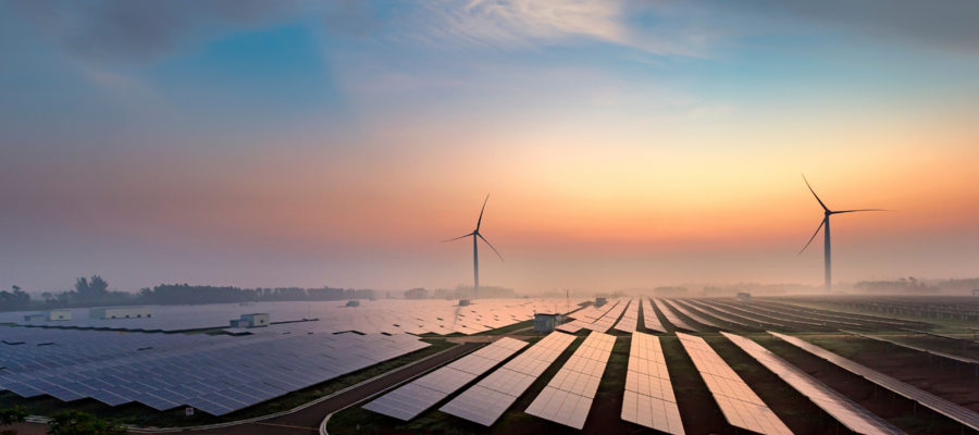 A field of solar panels, with wind turbines in the background