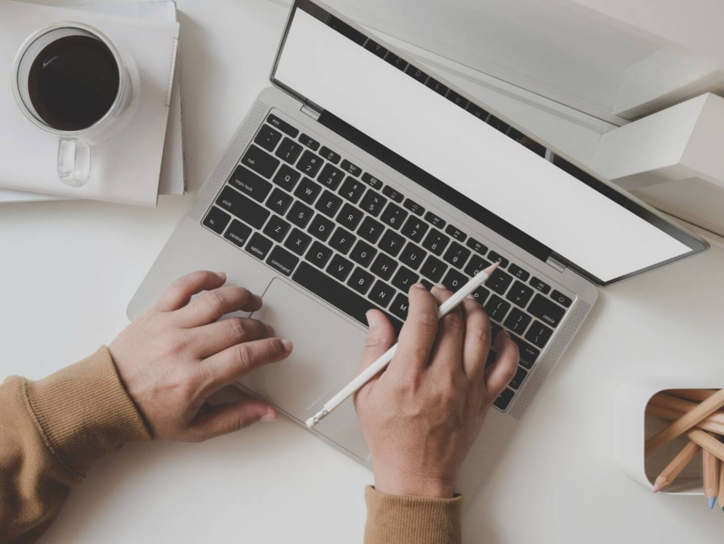 A bird's eye view of a laptop on a table, next to a coffee cup and a pot of pencils