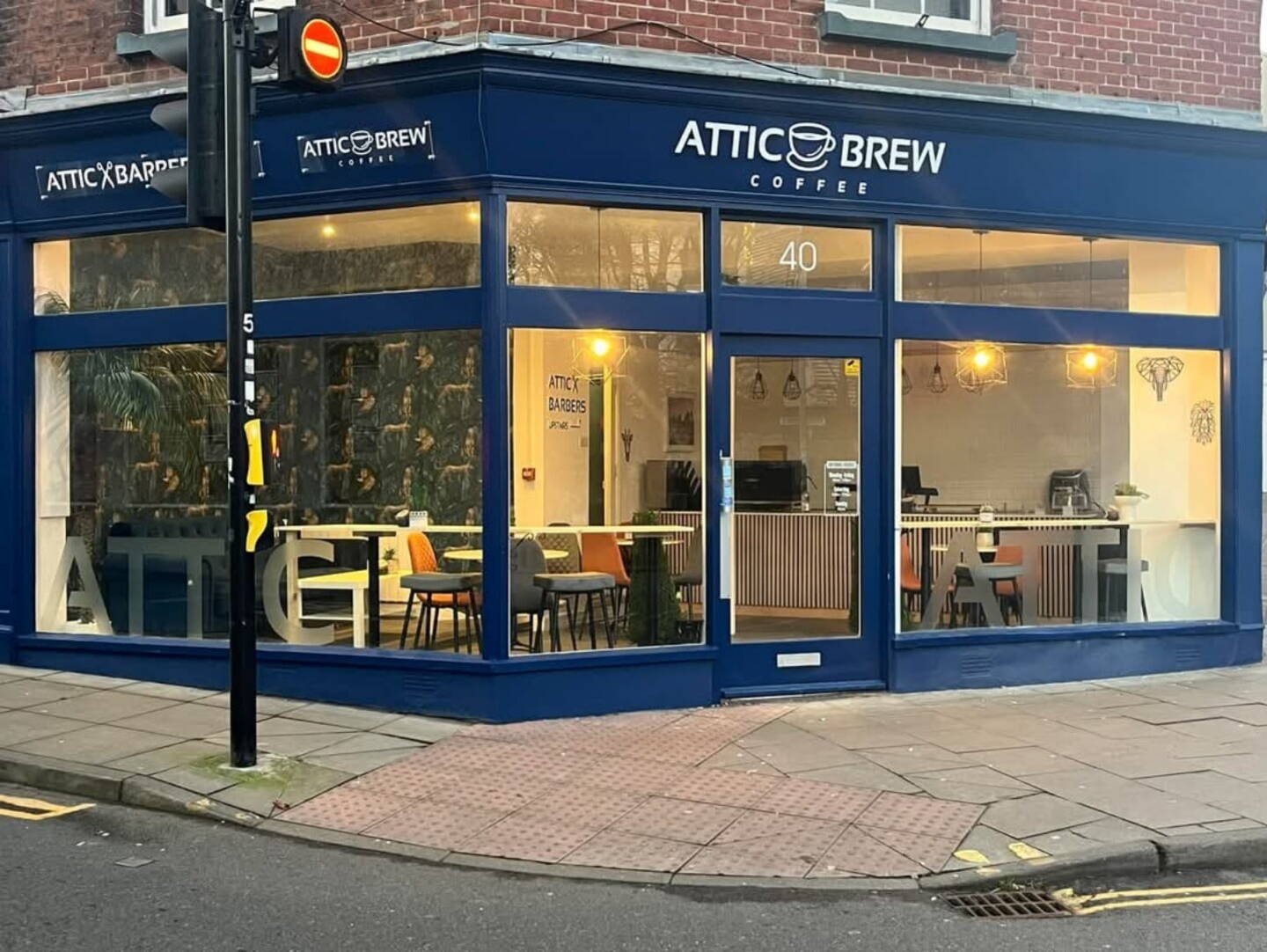 An image of Attic Brew, showing the exterior facade, from across the street. The building has large windows, framed by blue painted wood, with red bricks on the upper levels